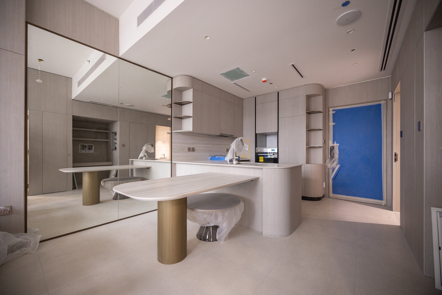 Pearl House By Imtiaz Modern kitchen interior featuring light wood cabinetry, a mirrored wall, and a blue door, reflecting a minimalistic design.